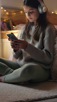 Teen girl using smartphone with headphones at home, vertical footage