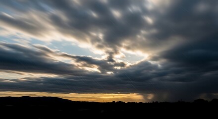 Obraz premium A dark cloudy sky during sunset over silhouette landscape