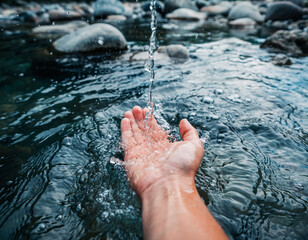 Hand dipping into cold refreshing mountain stream water with smooth stones