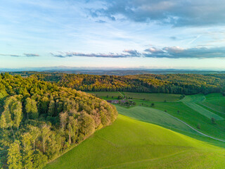 Aerial view of rolling hills and forested landscape at sunset in a serene rural area © YouraPechkin
