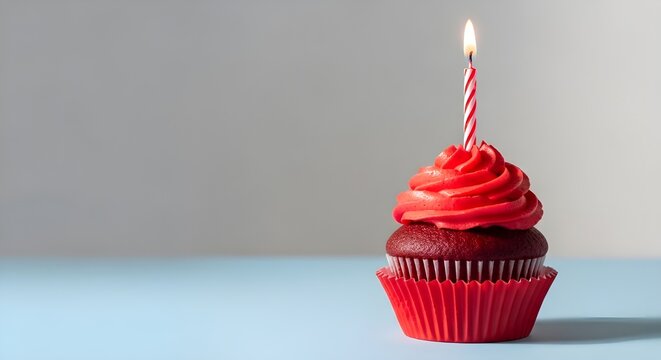 A chocolate cupcake with red frosting and a lit candle on top for a birthday celebration