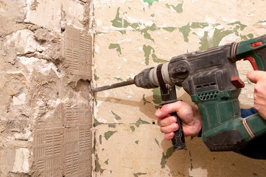 A worker knocks down old plaster and cement using a jackhammer.