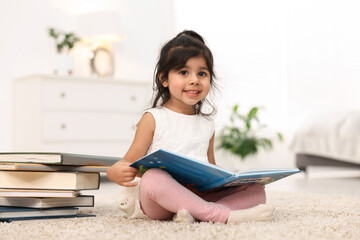 Fototapeta premium Cute little girl reading book on floor at home