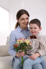 Little boy greeting his mom with flowers on sofa at home