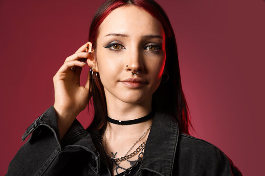 Portrait of beautiful young woman with piercings and stylish accessories in red light on pink background