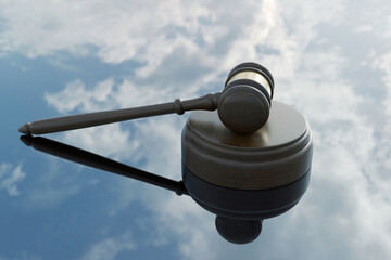 Wooden judge gavel and sound block resting on a reflective mirror surface with a blue sky and white clouds background. Symbol of legal justice, law, and authority in a bright conceptual setting.