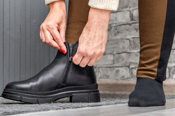 A woman puts on a black leather boot, close-up. A woman zips up her black boots. a woman unfastens her boot.  © Oleg Opryshko