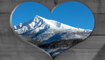 Massive wooden panel with a precisely carved heart revealing a snow-covered rocky mountain peak in...