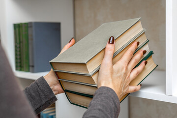 a woman puts a stack of books on a shelf. a woman arranges books on a bookshelf. female hands holding a stack of books.  © Oleg Opryshko