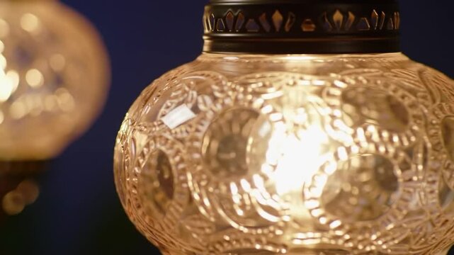 A close-up view presents ornate, glowing glass fixtures with intricate patterns. A second fixture glows softly in the background. The scene is illuminated by warm light