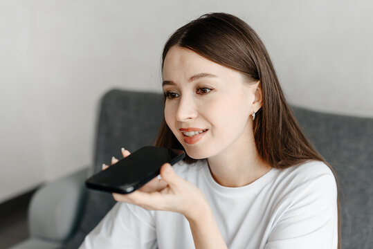 young beautiful caucasian brunette woman recording voice message, smiling widely, casual clothes, white T-shirt, talking by smartphone