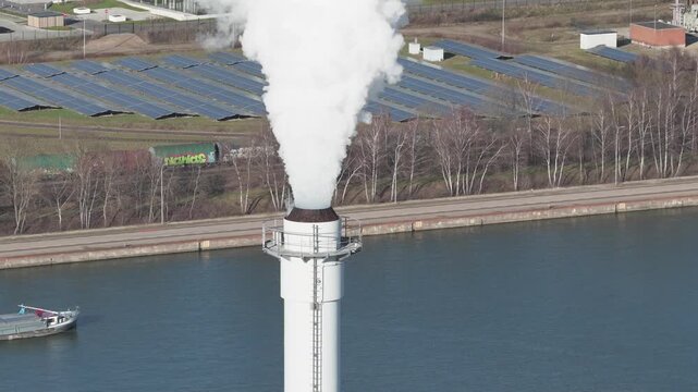 25 february 2026, Genk, Belgium. Aerial, orbit around smoking Industrial Chimney Near Canal with Cargo Barge &ndash; CO2 Emissions, Climate Change and Inland Shipping Concept. Air polution, co2 emission. En