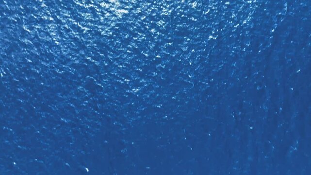 太陽が煌めく深い青の海面｜ドローンによる真上からの抽象的な波のテクスチャ