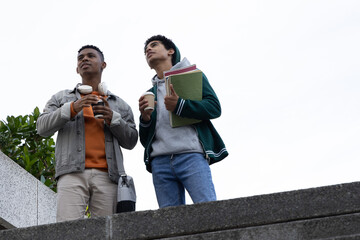 Two adolescent male students in hoodies standing on campus ledge holding coffee and notebooks © wavebreak3