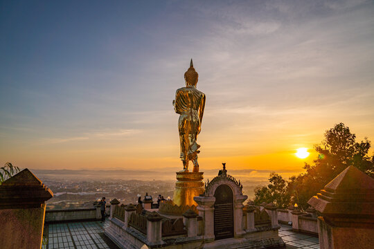 1. A golden standing Buddha faces the rising sun at Wat Khao Noi, glowing gently as morning light spreads across the horizon above Nan city.