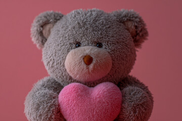 Obraz premium Adorable plush gray bear holding a soft pink heart pillow with a warm and cozy expression against a solid pastel pink background for love themes