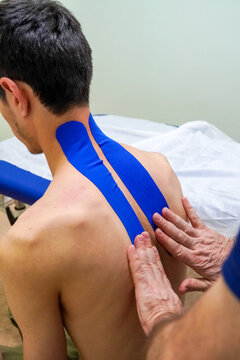Physiotherapist treats patient neck, back pain with kinesio tape close up. Unrecognizable young caucasian patient.Doctor examining her patient back in medical office