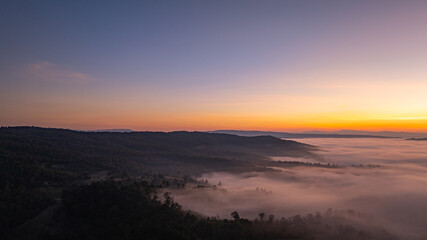 A breathtaking sunrise casts warm golden light over a mist-covered forest and rolling hills, creating a serene and atmospheric landscape scene. Ideal for themes of nature, tranquility,  © Narong Niemhom