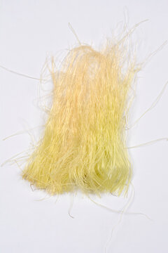 A vertical shot shows an isolated small pile of fine, pale yellow corn silk fibers resting on a plain white background with trailing, wispy strands
