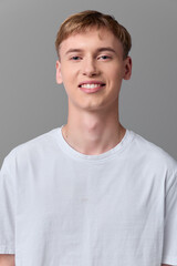 Young man in a white t shirt smiles softly against a neutral backdrop, ideal for lifestyle and wellness themes, casual headshot style focusing on approachable, friendly appeal.