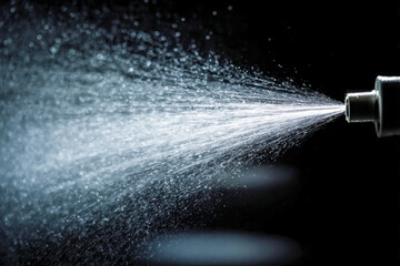 Naklejka premium Spray from a nozzle dispersing fine mist droplets into the air against a dark background with detailed water particle texture