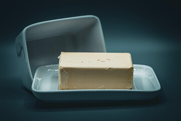 A solid block of fresh yellow butter sits on a white ceramic dish with its lid propped open. The...