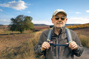Senior Man Hiking Outdoors With Backpack In Open Countryside, Wearing Cap And Sunglasses © villorejo