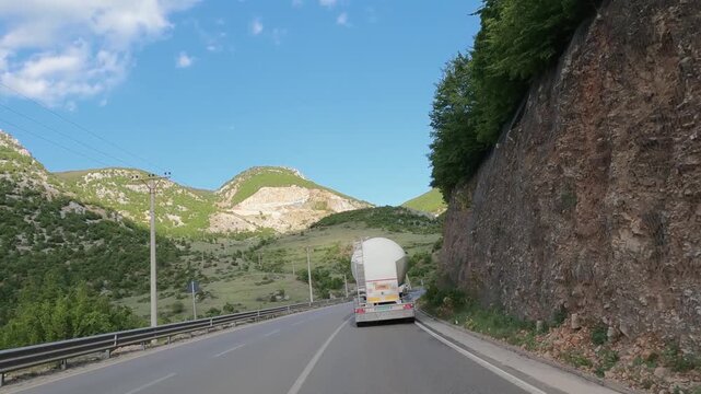 Tank cistern truck driving on a scenic road through mountain landscapes under a blue sky