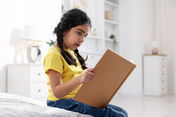 Fototapeta premium Cute little girl reading book on bed at home