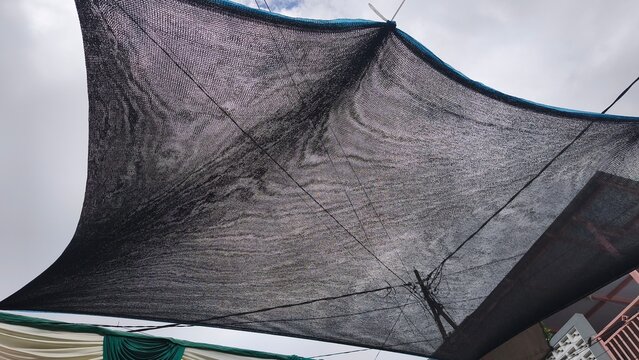 Black sunshade net or garden mesh canopy installed outdoors under an overcast sky for sun protection.