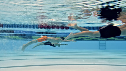 Underwater shot two swimmers in a pool during training. One wears orange flippers, practicing a stroke, while the other is nearby, both engaged in swimming exercises. © stockcopter