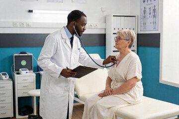 Obraz premium A male doctor examines an elderly woman with a stethoscope in a medical office.