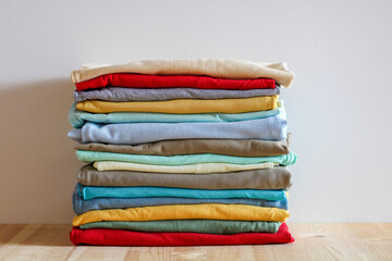 Stack Of Colorful Folded Clothes On Wooden Table Against Neutral Background, Organized Wardrobe Concept, Home Laundry And Minimal Lifestyle