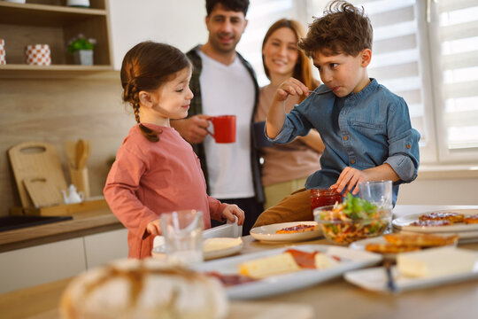 Boy tasting jam from spoon during family breakfast