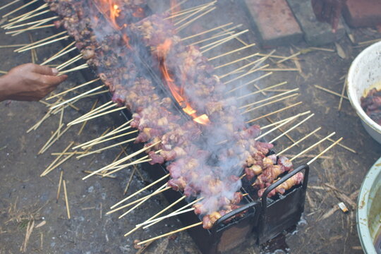 Indonesian lamb satay grilling on a charcoal brazier with smoke and hot flames at a street market.