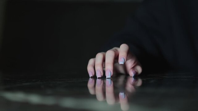 Woman hand with polished nails tapping a reflective surface with soft lighting showing gesture of boredom