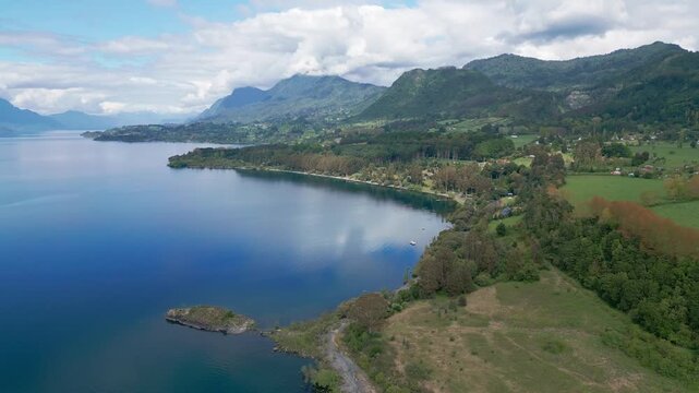 Orbit shot over lakeside village with calm bay and forested mountain backdrop. Lago Ranco, Chile