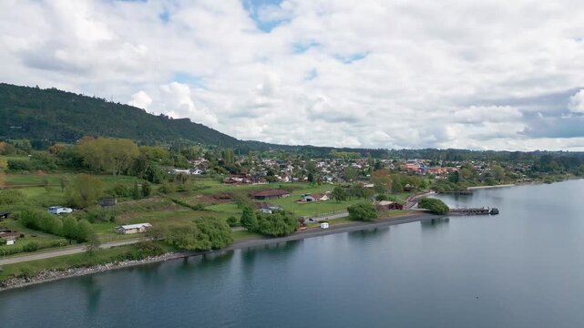 Ascending tilt down over lakeside town with pier and forested hillside. Lago Ranco, Chile