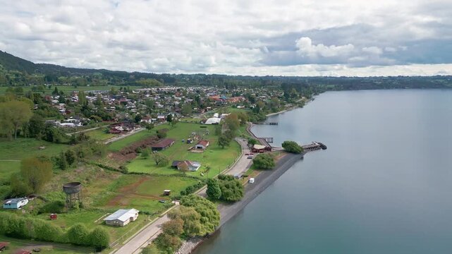 Forward flight over lakeside town with pier and waterfront along calm shore. Lago Ranco, Chile
