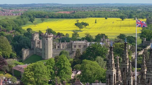 Drone reveal of Warwick Castle, moving from the Dungeon to St Mary&rsquo;s Belfry with the England flag waving, showcasing medieval architecture and surrounding village scenery.