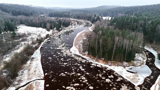 Aerial view of a frozen river full of floating ice floes meandering through the woods.