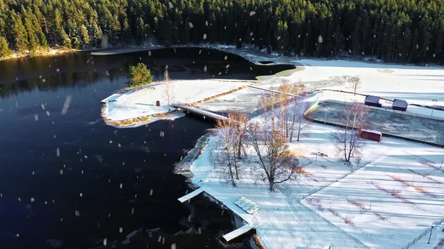 Snow covered island and lakeside are with ice ring on sunny winter day aerial view