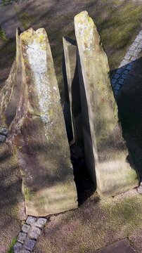 Stanstead Abbotts memorial vertical drone orbit descent over stone sculpture on circular paved plaza with long tree shadows, dramatic winter sunlight, Hertfordshire, England, UK.