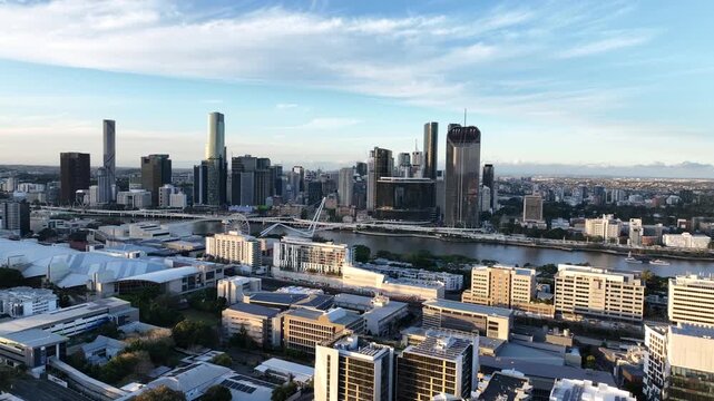 Slow drone side tracking at golden hour over South Bank, revealing Queens Wharf and The Star Brisbane towers along the Brisbane River with Neville Bonner Bridge, Brisbane, QLD, Australia