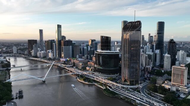 Slow drone tracking along the Brisbane River at golden hour, moving past Queens Wharf and The Star Brisbane toward the CBD skyline and Neville Bonner Bridge, Brisbane, QLD, Australia