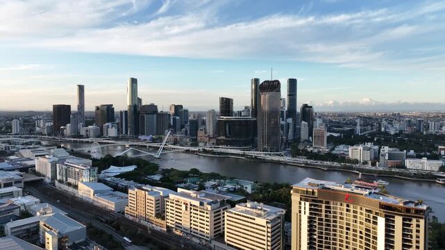 Slow drone pan left at golden hour across the Brisbane River, bringing Queens Wharf and The Star Brisbane towers into focus with Neville Bonner Bridge and the CBD skyline, Brisbane, QLD, Australia