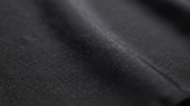 Closeup macro shot of a dark grey textured fabric with subtle folds and a seam running diagonally across the frame showcasing its detailed surface and material properties.
