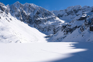 Obraz premium Czarny Staw Gasienicowy lake in Gasienicowa Dolina valley in winter in Tatra Mountains. Mountain winter landscape with frozen lake. High Tatras, Poland