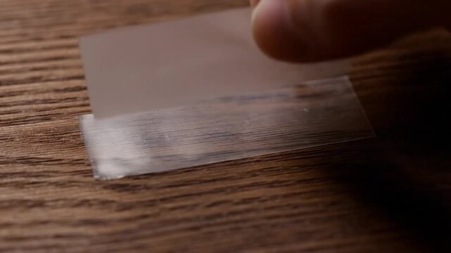 A hand peels a sticker from a wooden surface, close-up with light and shadow