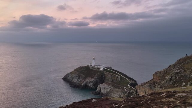 Aerial drone footage of South Stack Lighthouse on the rugged Welsh coast, dramatic cliffs and Atlantic waves, cinematic seascape ideal for travel, nature, coastal tourism and documentary use.